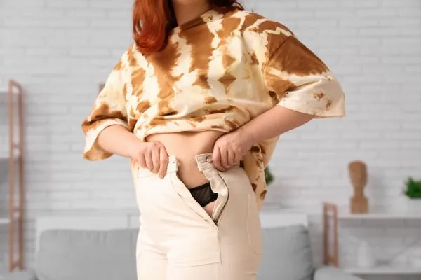 Image of woman trying to do her trousers up after pregnancy weight gain Malmesbury